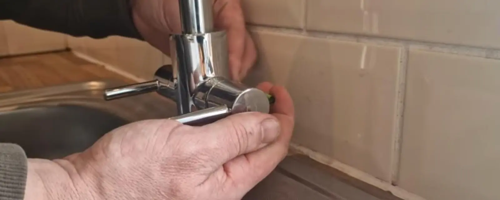 Hands repairing a chrome kitchen faucet