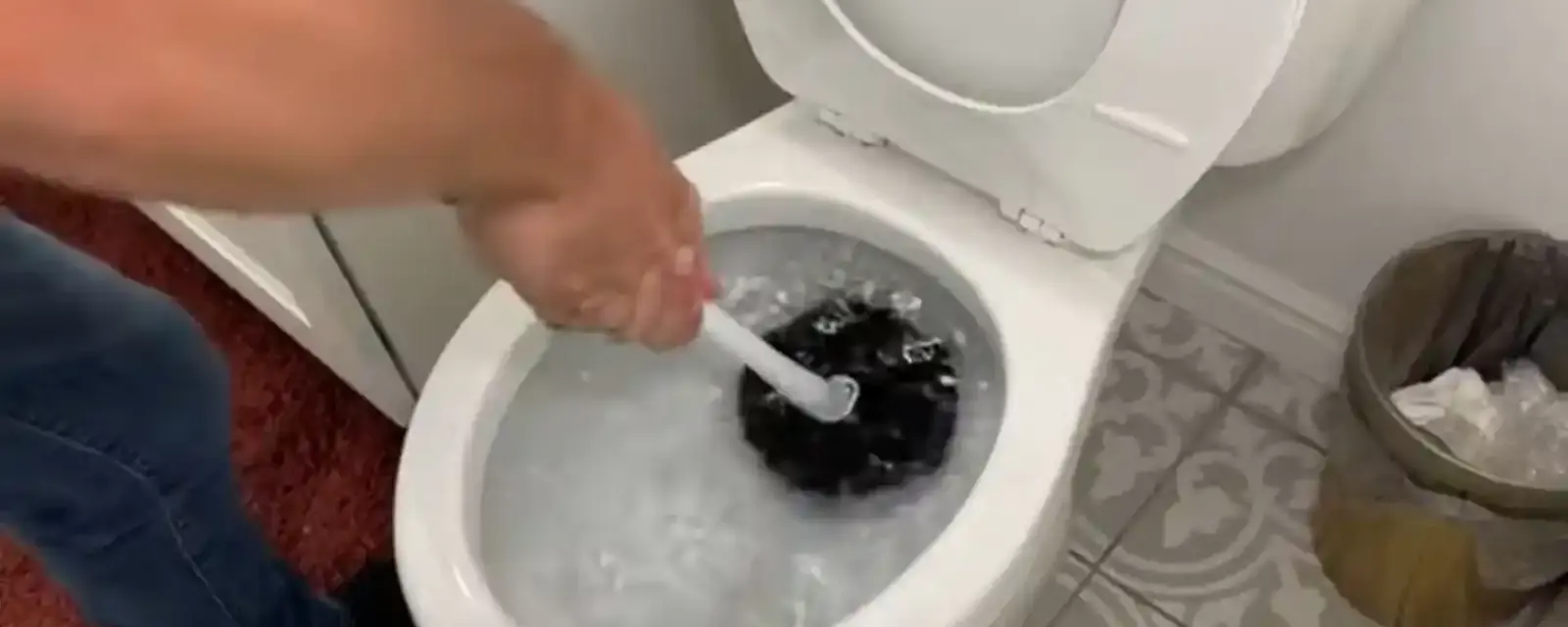 Hand using a toilet plunger in a clogged bowl