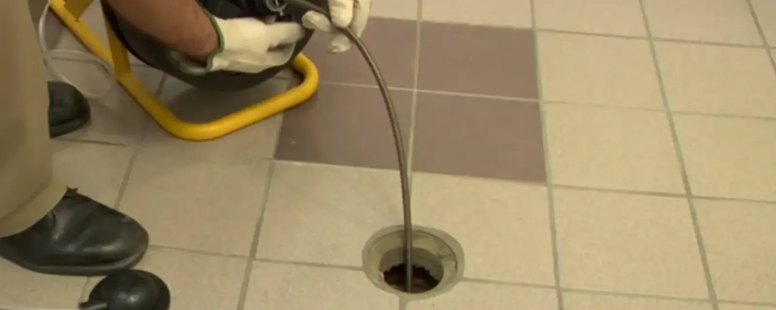 Plumber feeding a drain cable into a tiled floor drain