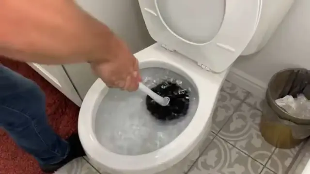 Hand using a toilet plunger in a clogged bowl