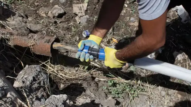 Plumber connecting a new water line in a dug trench