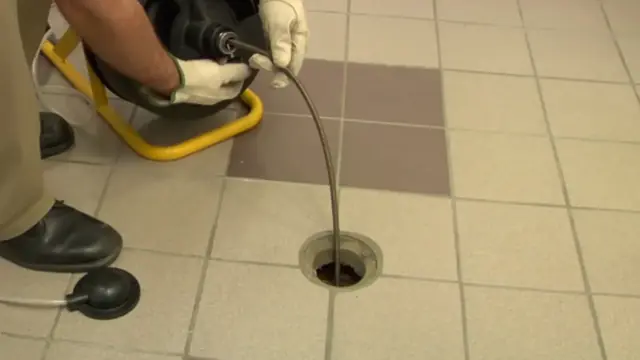 Plumber feeding a drain cable into a tiled floor drain