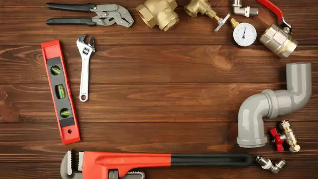 Level, pipe wrench and pipe fittings laid out on a wooden surface